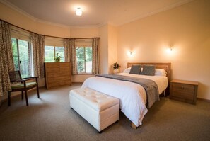 A bedroom with a large bed, a nightstand, a dresser, a chair, and a window with curtains.