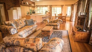 A living room with patterned sofas, a coffee table, and a television on a wooden cabinet. - Whispering Karri Retreat | 5-Acre Hideaway (Shadforth)