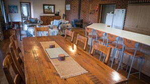 A spacious dining area with a long wooden table, surrounded by chairs, in a room with a brick wall and a fireplace. - Whispering Karri Retreat | 5-Acre Hideaway (Shadforth)