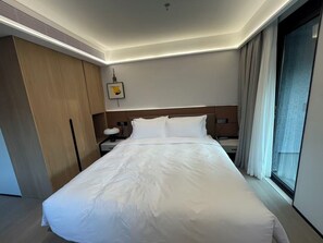 A hotel room with a large bed, a wooden wardrobe, a bedside table with a lamp, and a window with curtains. - Nester Finn Suites Entertainment Toronto (Toronto)