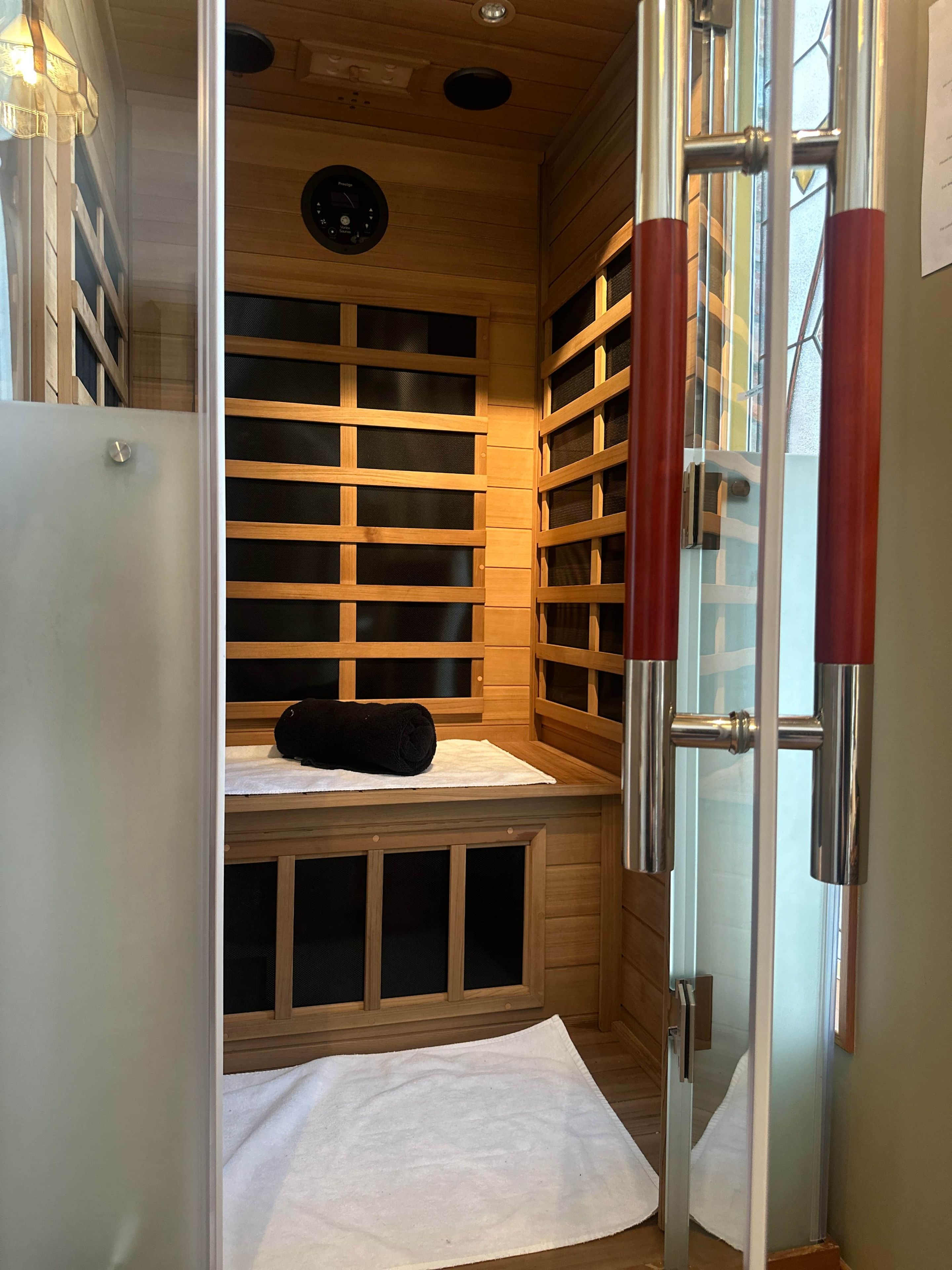 A sauna with wooden benches, a glass door, and a towel on the floor.
