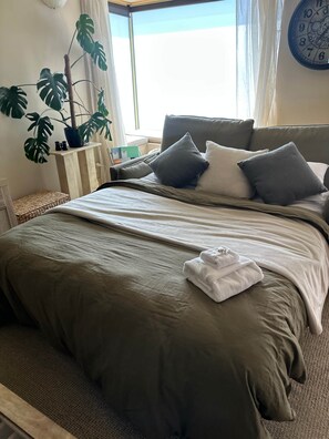 Una cama bien hecha con una colcha verde, almohadas y una toalla blanca doblada.