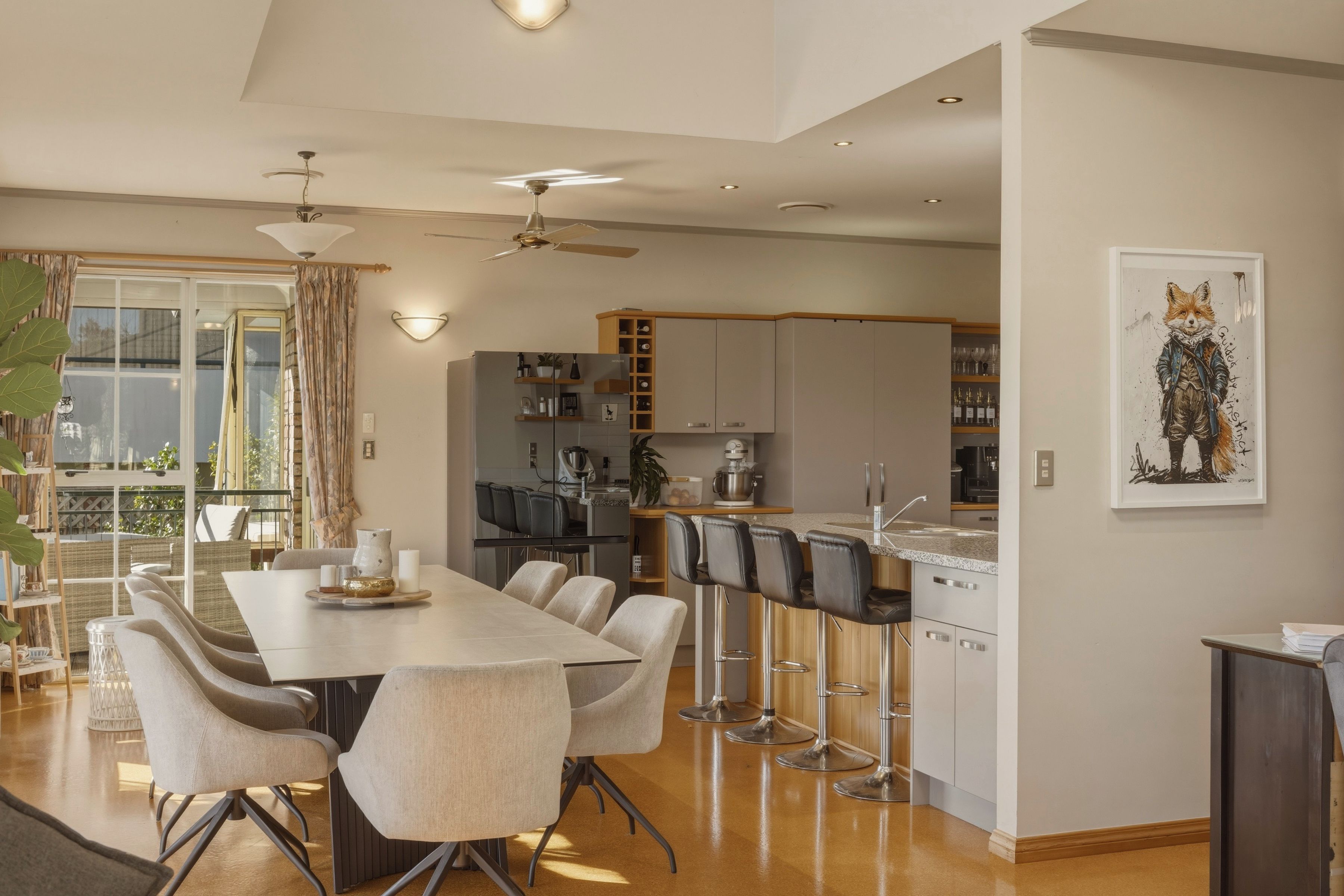 A modern kitchen with a dining area, bar stools, and a large window.