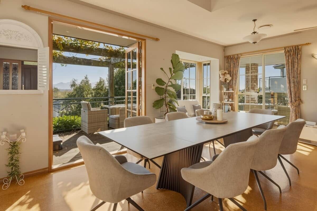 A dining area with a large table and chairs, large windows, and a view of the outdoors.
