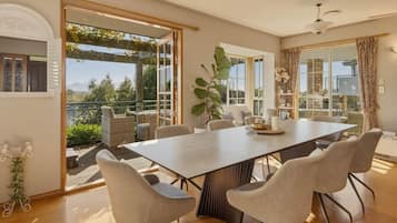 A dining area with a large table and chairs, large windows, and a view of the outdoors.