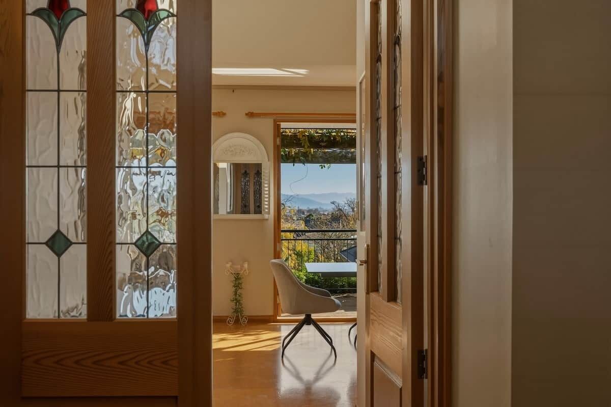 A room with a view through a window, a chair, and a door leading to another space.