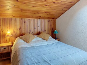 Um quarto com painéis de madeira, uma cama, dois travesseiros, uma mesinha de cabeceira com abajur e uma pequena mesa também com abajur.
