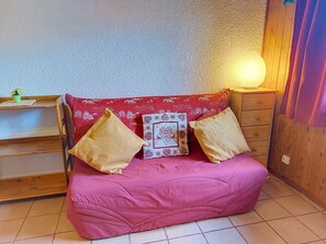 A pink bean bag chair with patterned cushions, a small table with a potted plant, and a wall-mounted lamp. - Les Grandes Aiguilles by Interhome (Saint Gervais)