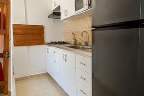 Eine Küche mit weißen Schränken, einem Edelstahl-Kühlschrank, einer Mikrowelle und einem Gasherd.