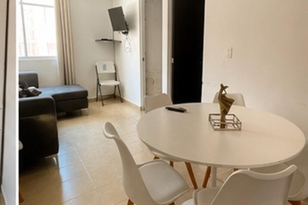 A room with a round white table, white chairs, a black sofa, and a white chair.