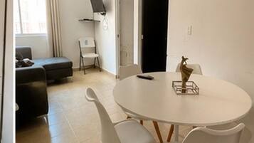 A room with a round white table, white chairs, a black sofa, and a white chair.