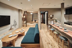Un interior moderno con una larga mesa de comedor, un sofá y una zona de cocina con taburetes.