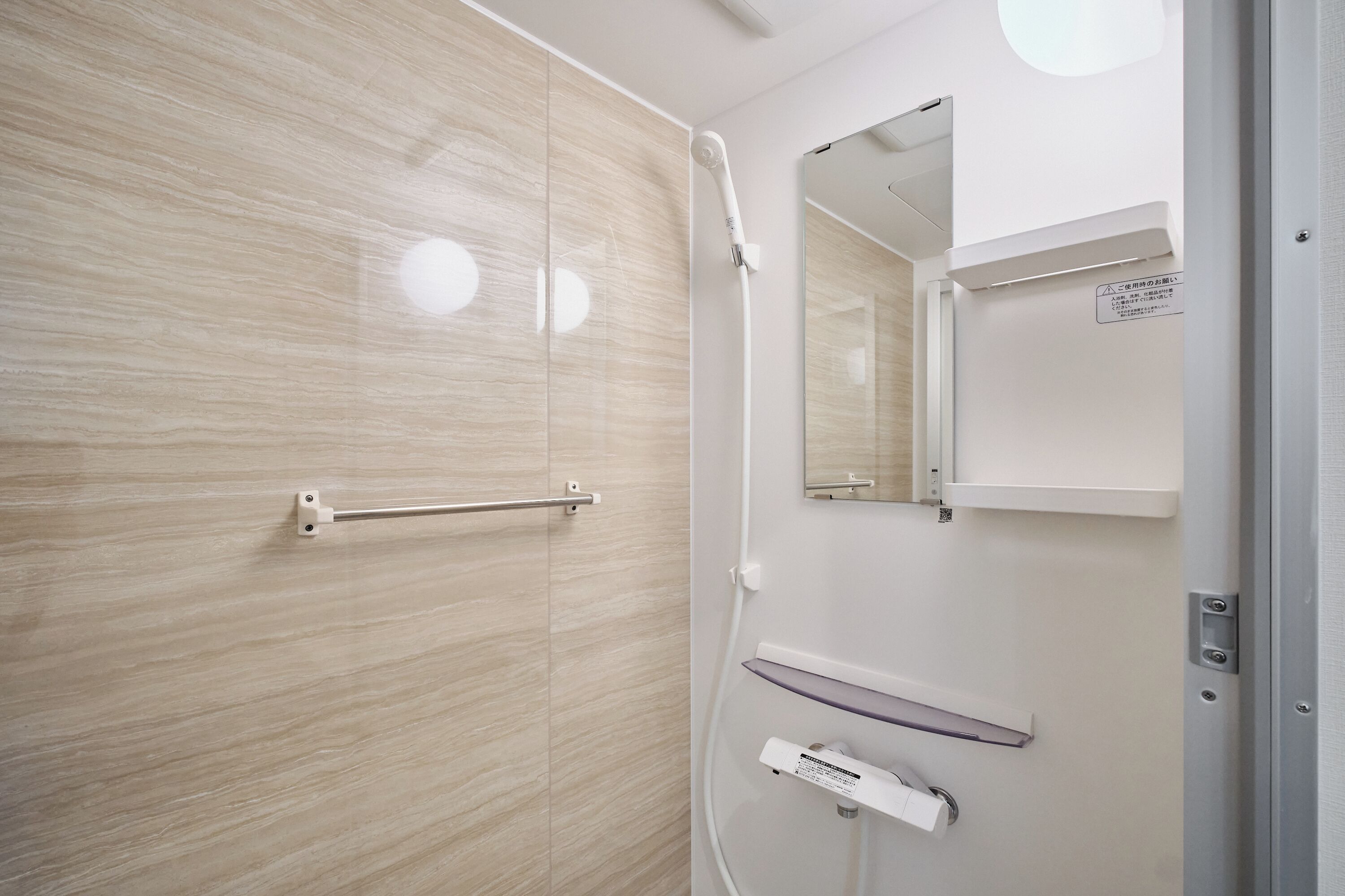 A modern bathroom with a glass shower enclosure, a handrail, a mirror, and a towel rack.