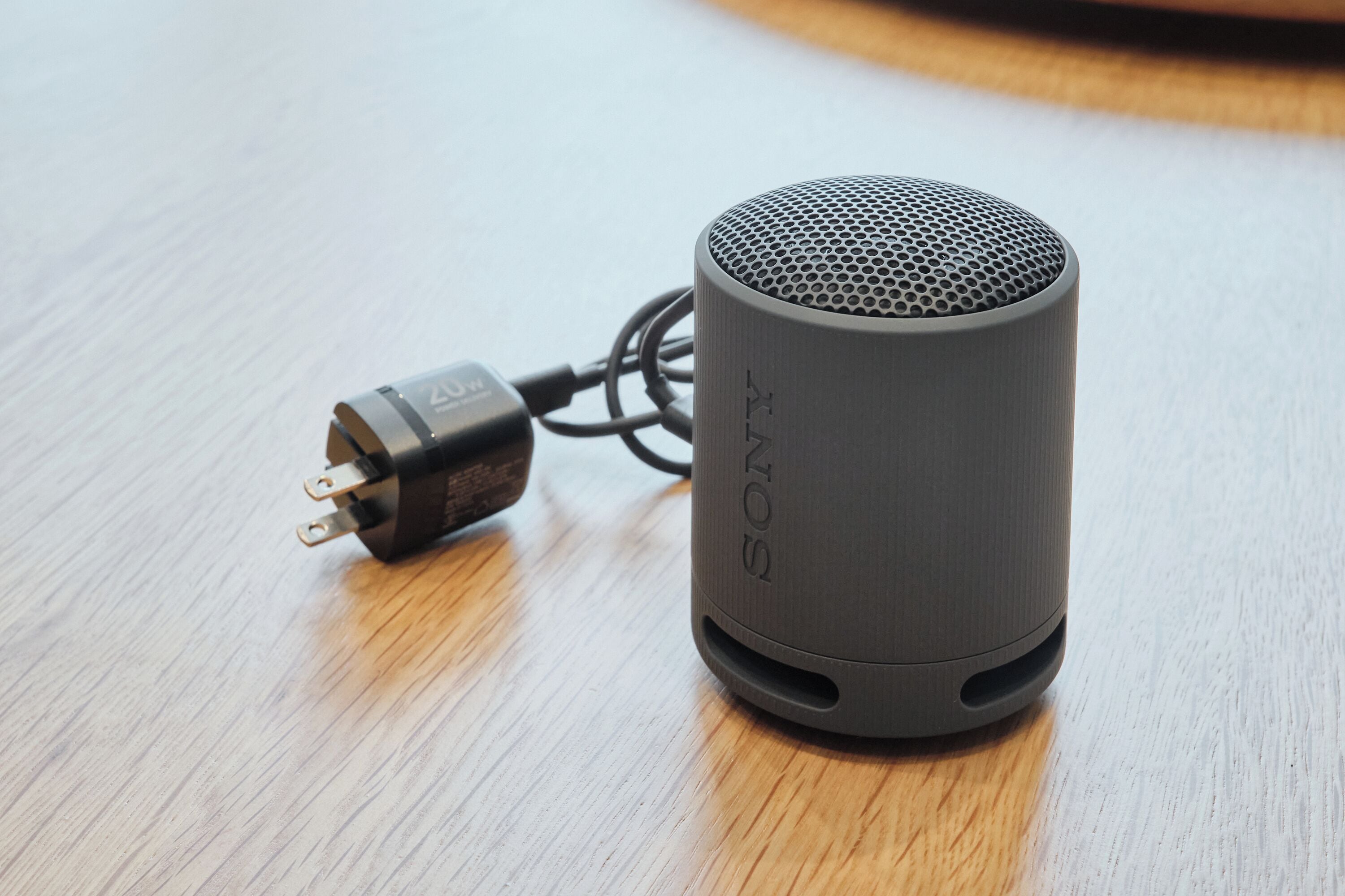 A Sony portable speaker with a power cord on a wooden surface.