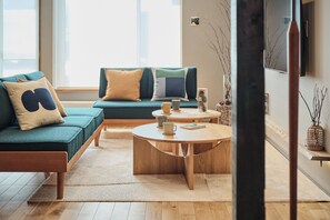 Una sala de estar moderna con un sofá color turquesa, una mesa de centro redonda de madera y un ventanal que deja entrar luz natural.