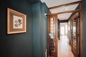 A hallway with a wooden door, a framed calligraphy piece, and a digital device on a stand.