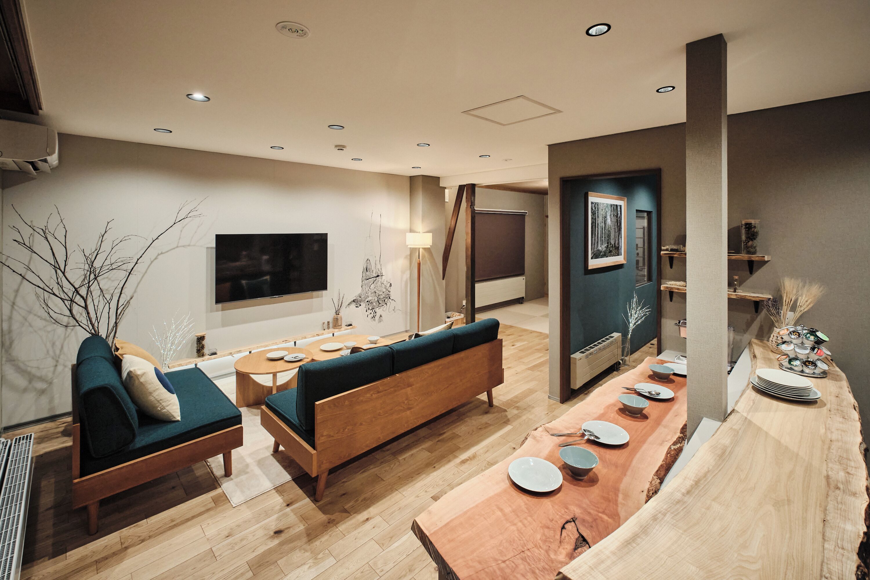 A modern living room with a sofa, a dining table set for four, and a TV mounted on the wall.