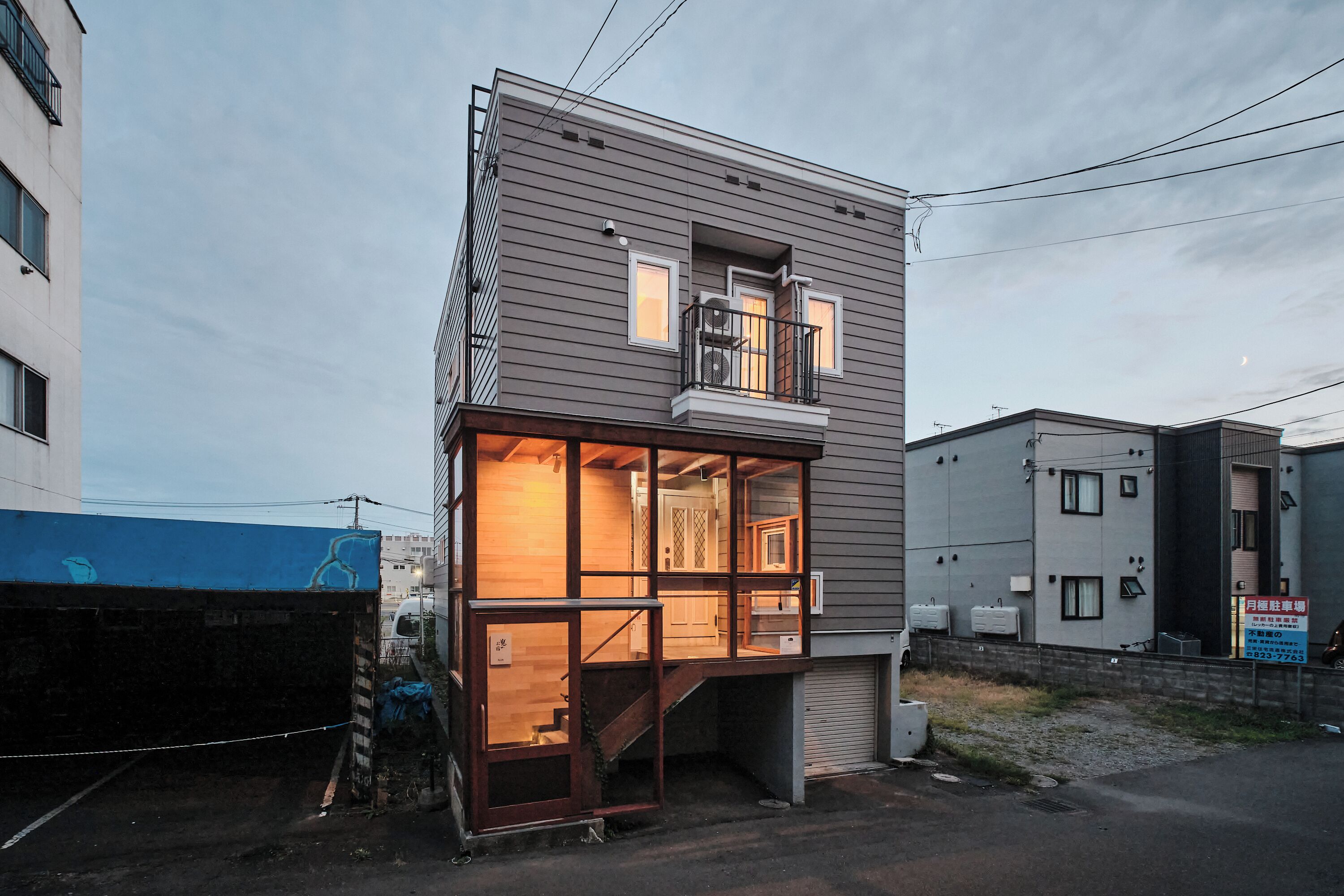 A modern two-story building with a glass facade, a visible staircase, and a small balcony.