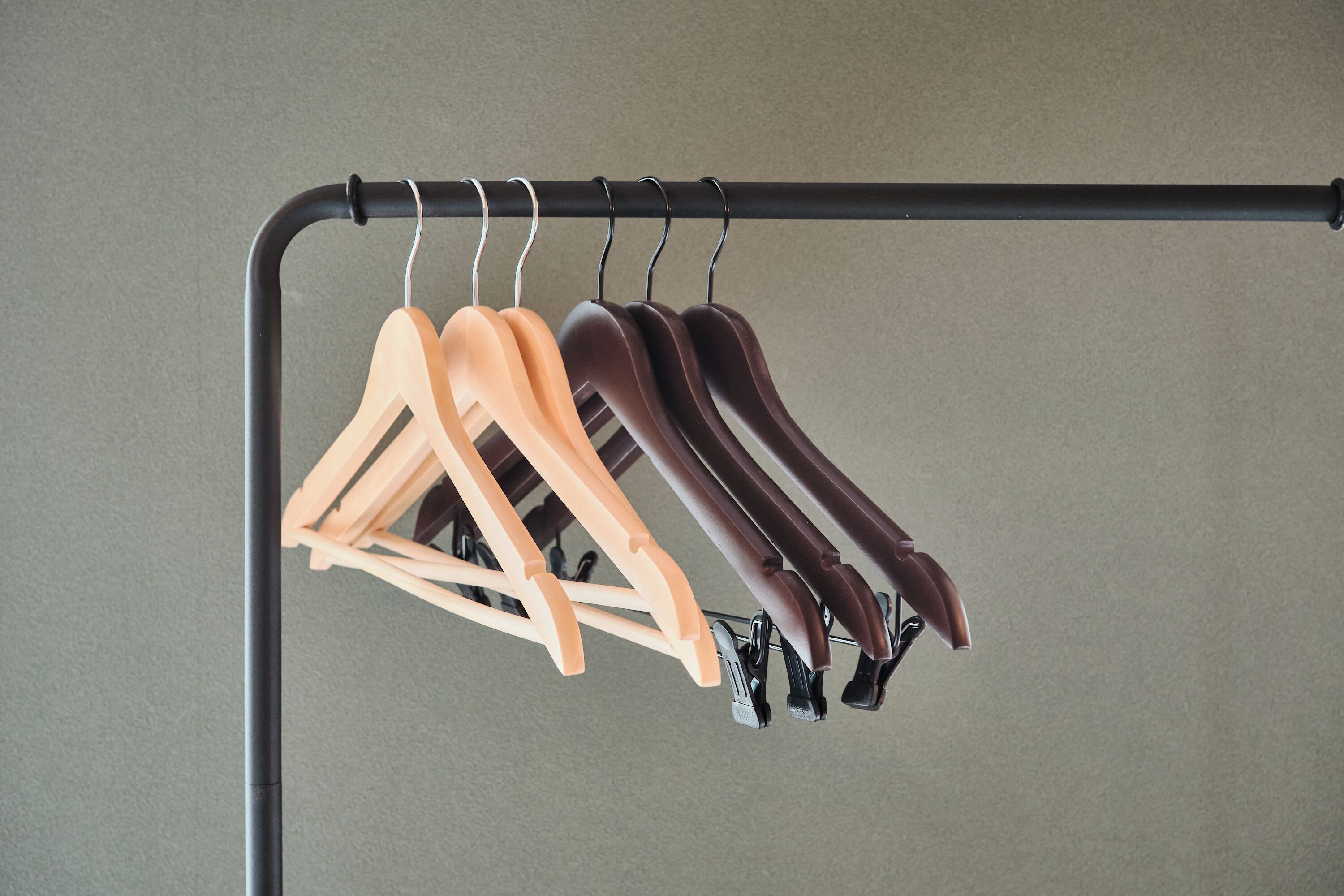 A clothing rack with multiple hangers against a plain wall.
