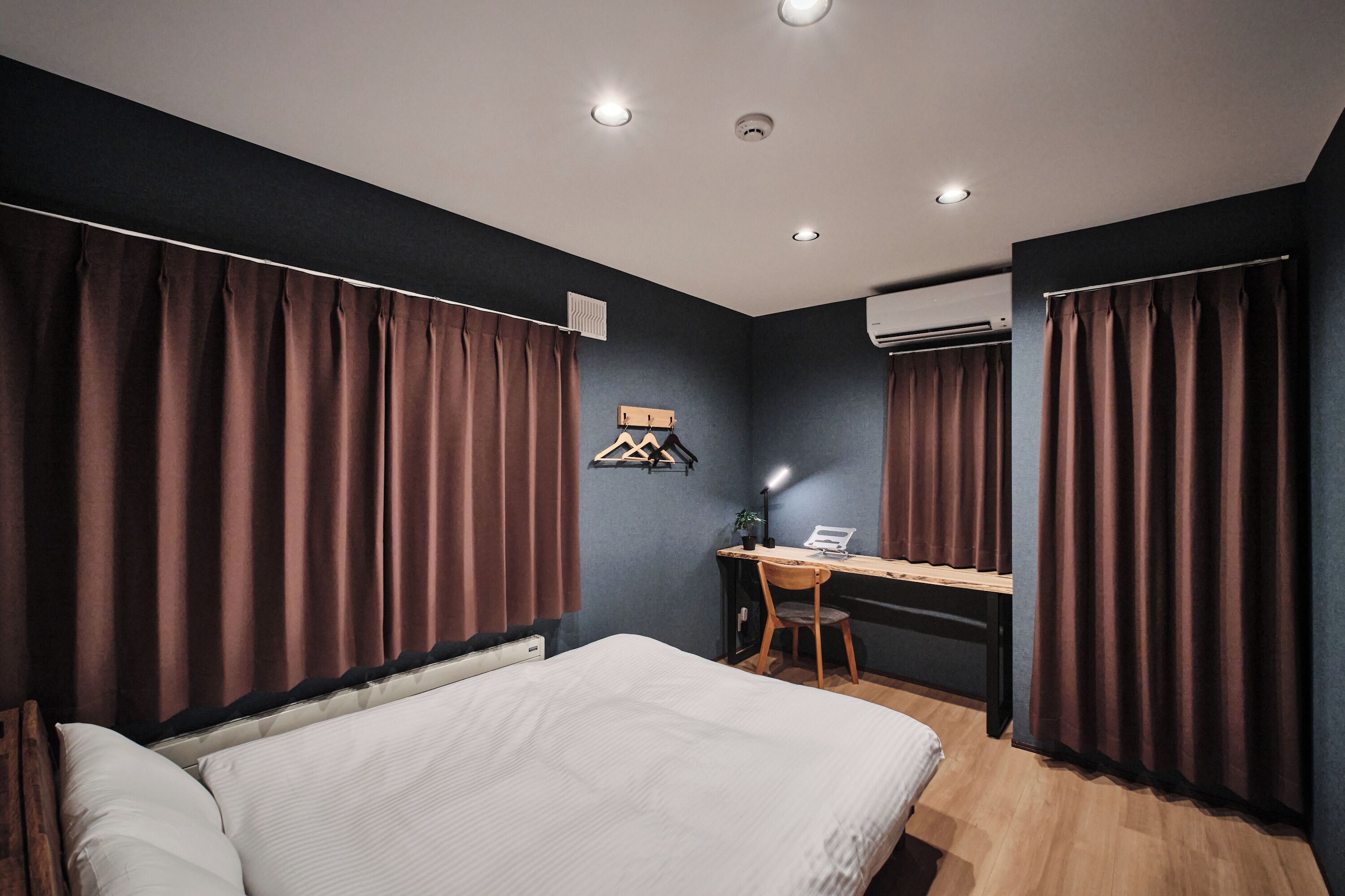 A hotel room with a bed, a desk, and a chair. There is an air conditioning unit on the wall.
