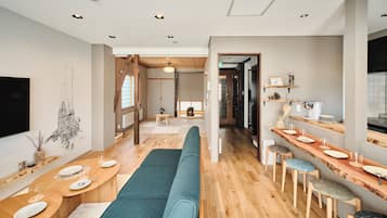 Un intérieur moderne avec un long banc en bois, un coin repas avec des tables et des chaises, et un espace cuisine doté d’un comptoir et de tabourets.