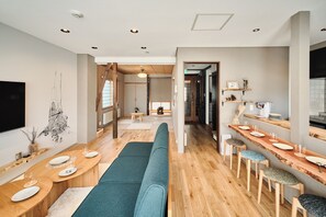 A modern interior with a long wooden bench, a dining area with tables and chairs, and a kitchen area with a counter and stools. - Kame no oyado VILLA Ecinke Sapporo (Sapporo)