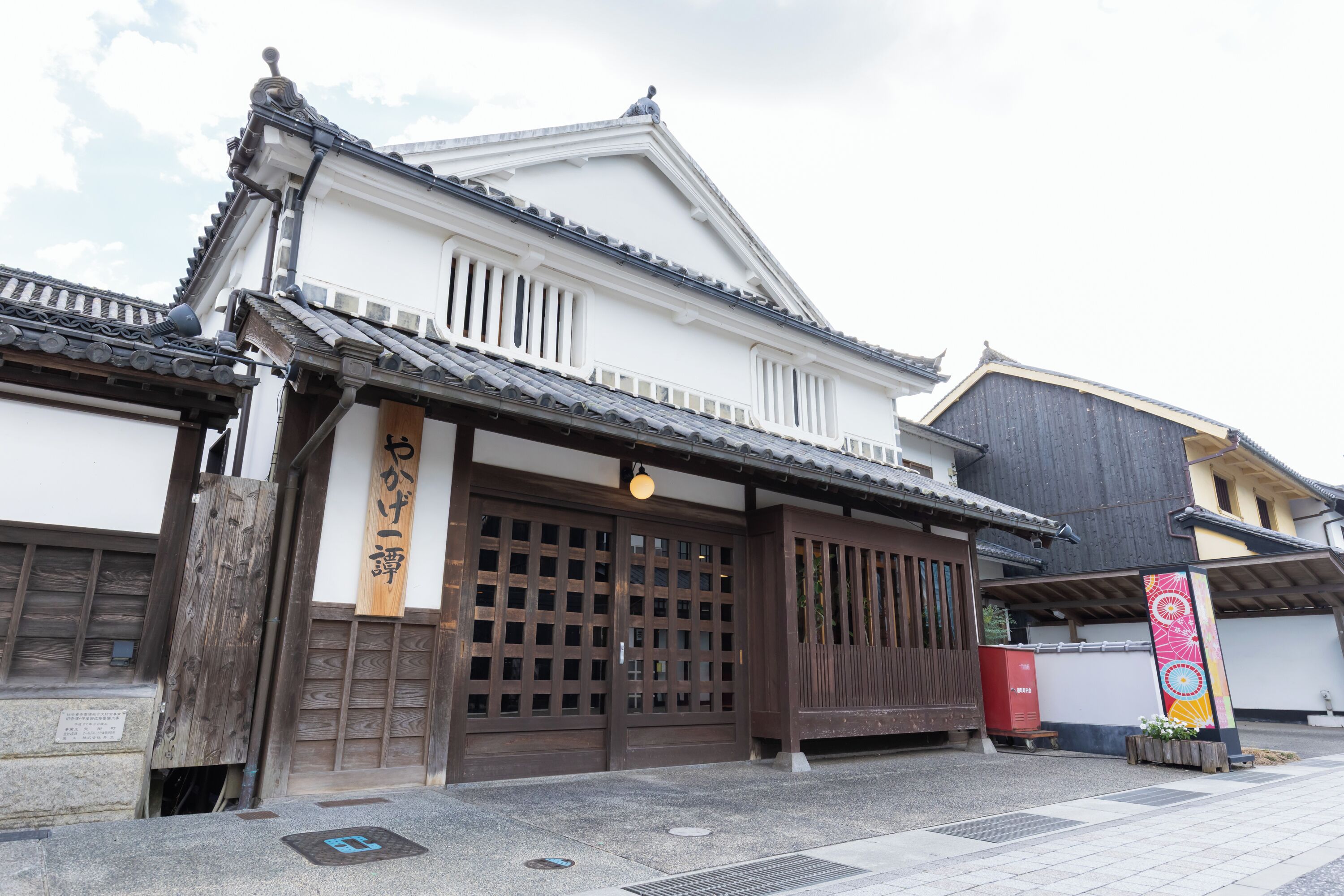 A traditional Japanese building with a wooden entrance gate, a tiled roof, and a signboard.