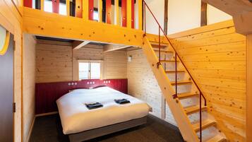 Una habitación con una cama, pared roja, ventana y escalera de madera.