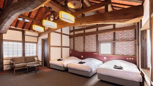 A room with a high ceiling, wooden beams, a sofa, two beds, and patterned wallpaper.