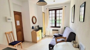 A room with a dining table, chairs, a sofa, a TV, and a window with curtains.