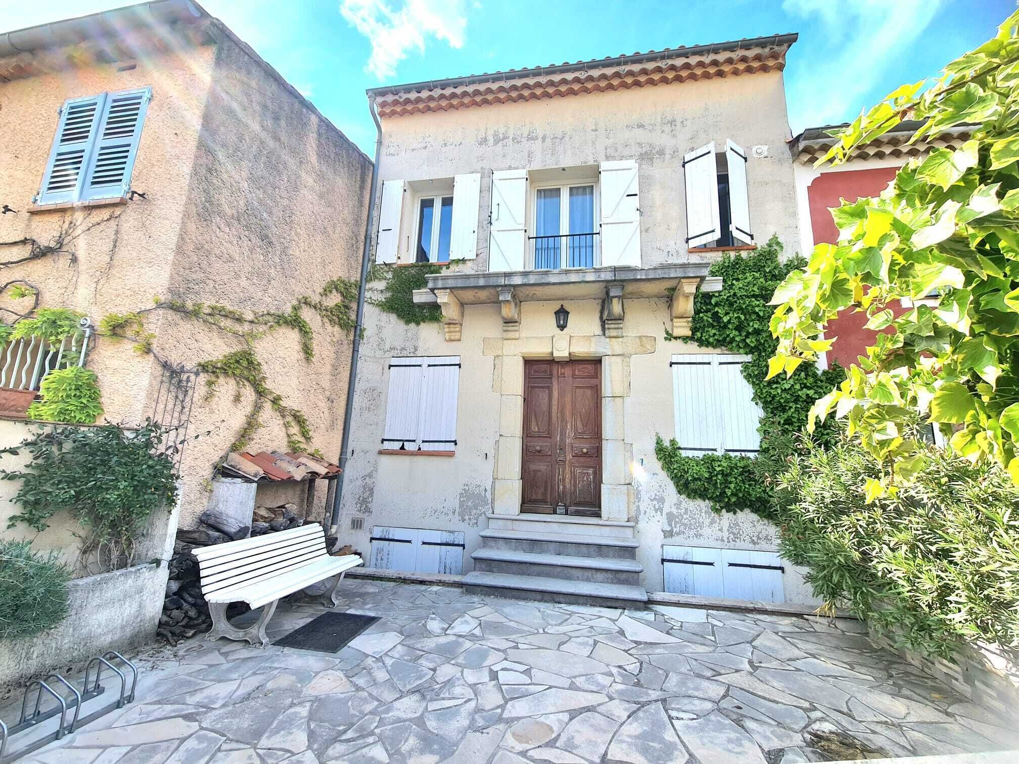 A courtyard with a stone floor, a wooden bench, and a building with a wooden door and shutters.