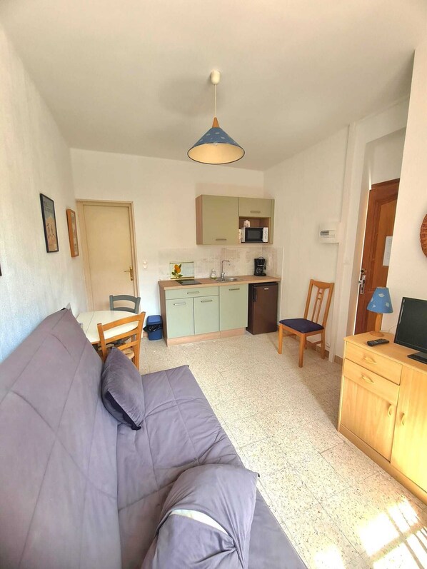 A compact living space with a kitchenette, a sofa, a chair, and a small table.