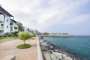 Un paseo marítimo costero con edificios modernos, un muro de piedra que protege la costa y una vista despejada del mar.