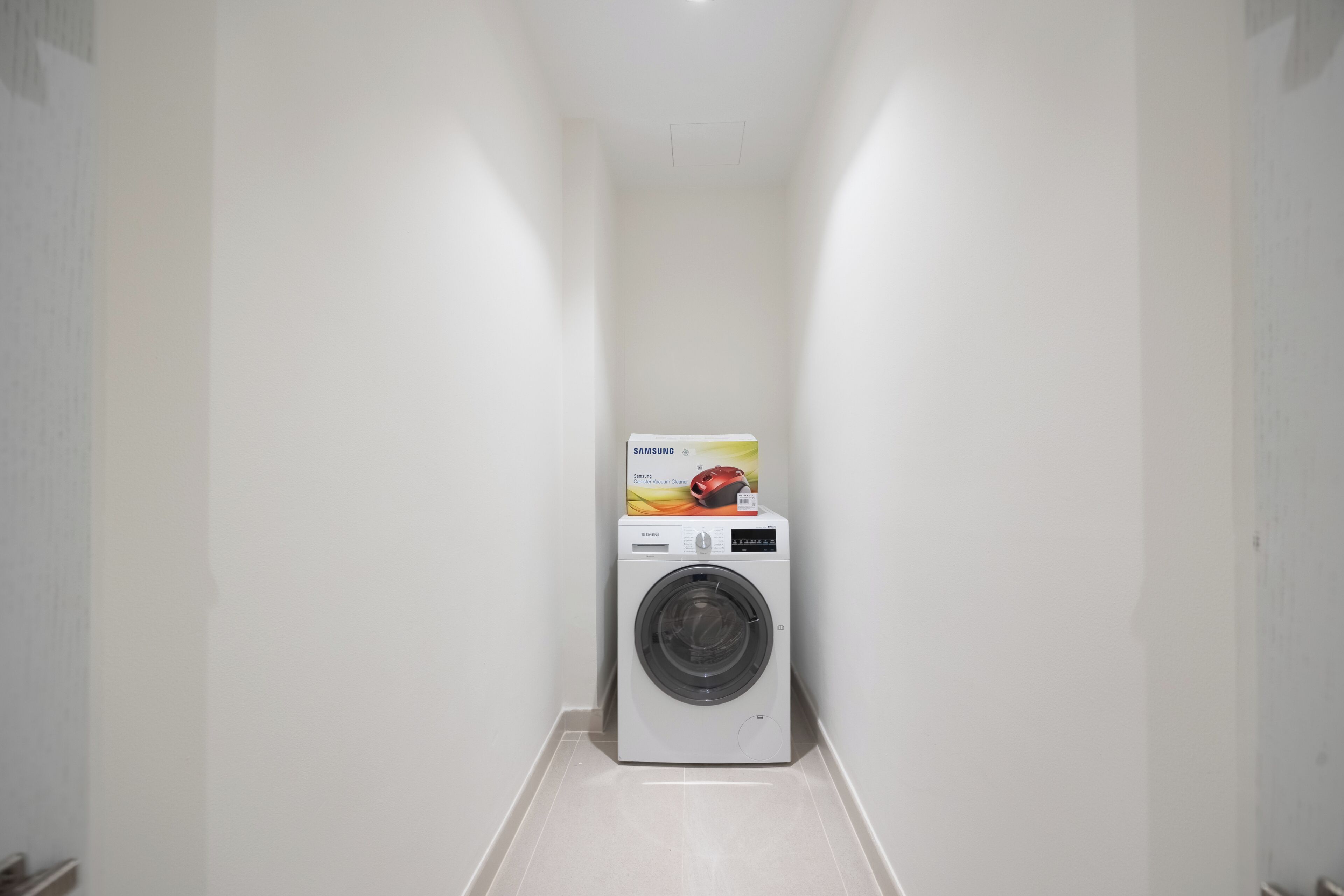 A laundry room with a white washing machine and a Samsung canister vacuum cleaner on top.