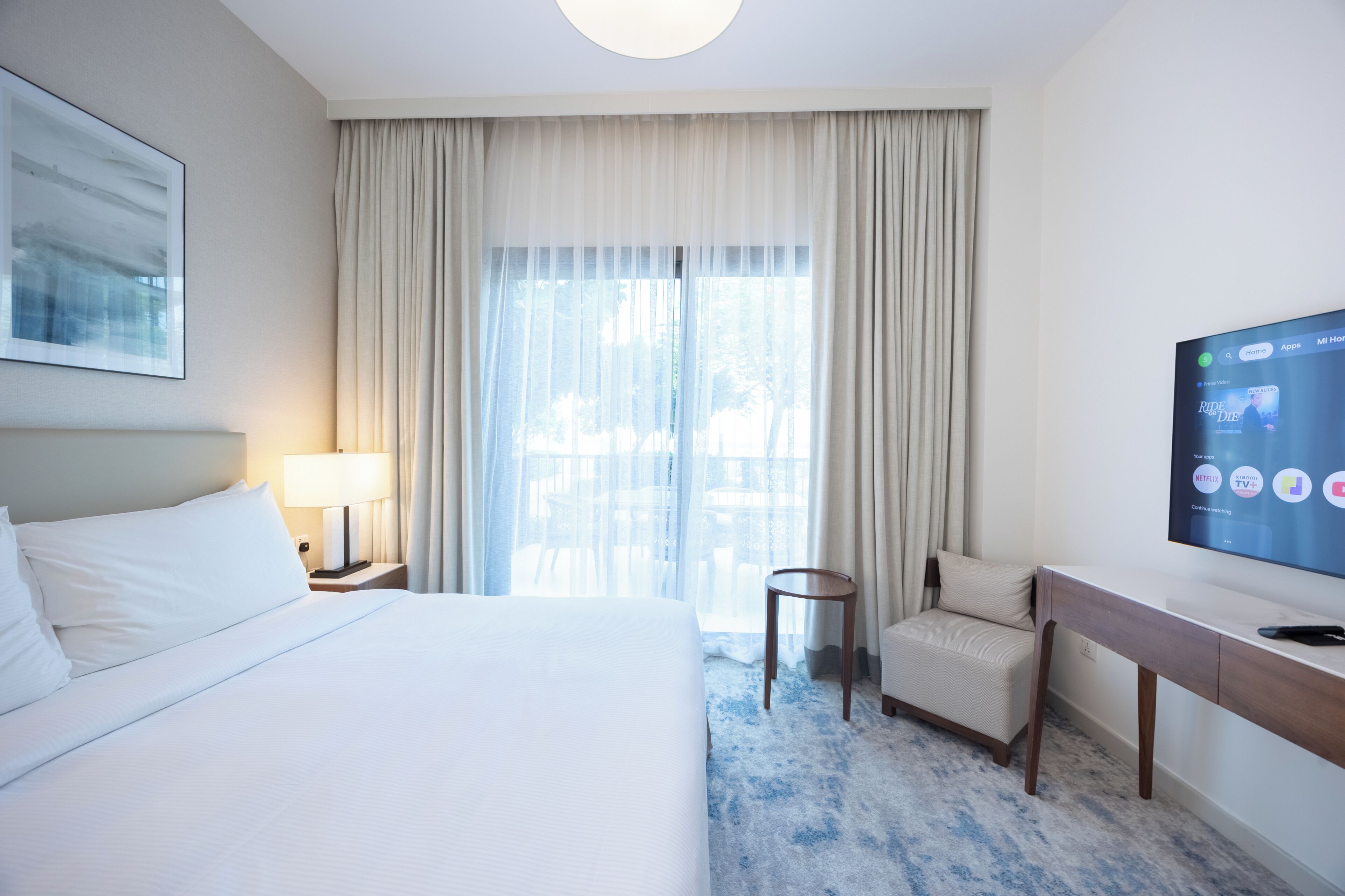 A hotel room with a bed, a desk, a chair, a television, and a window with curtains.
