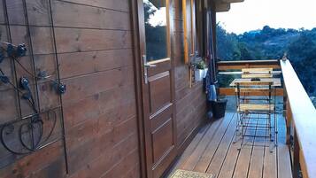 A wooden deck with a bench and potted plants, overlooking a hilly landscape.