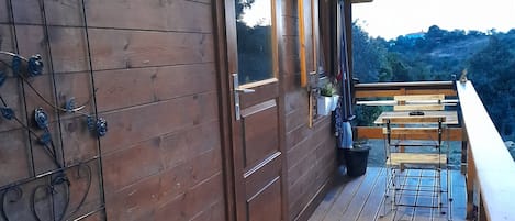 A wooden deck with a bench and potted plants, overlooking a hilly landscape.
