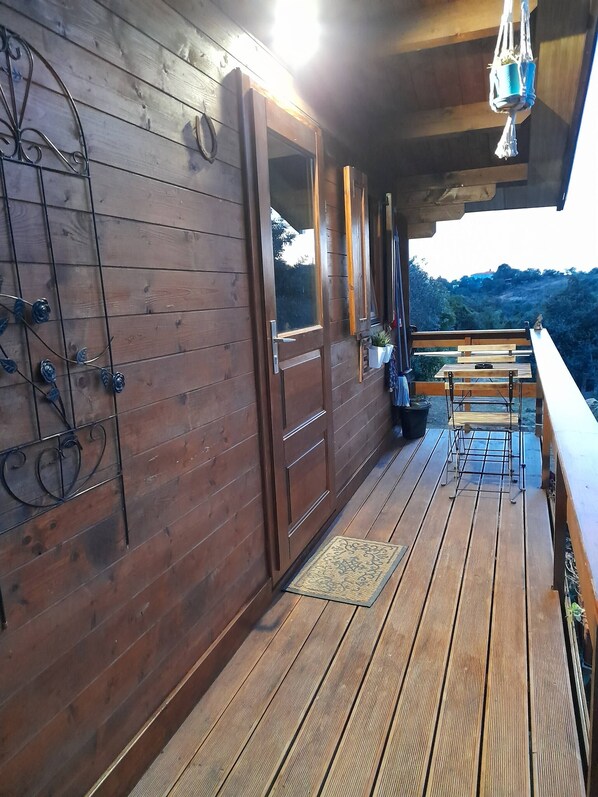 Una terraza de madera con un banco y plantas en macetas, con vistas a un paisaje montañoso.