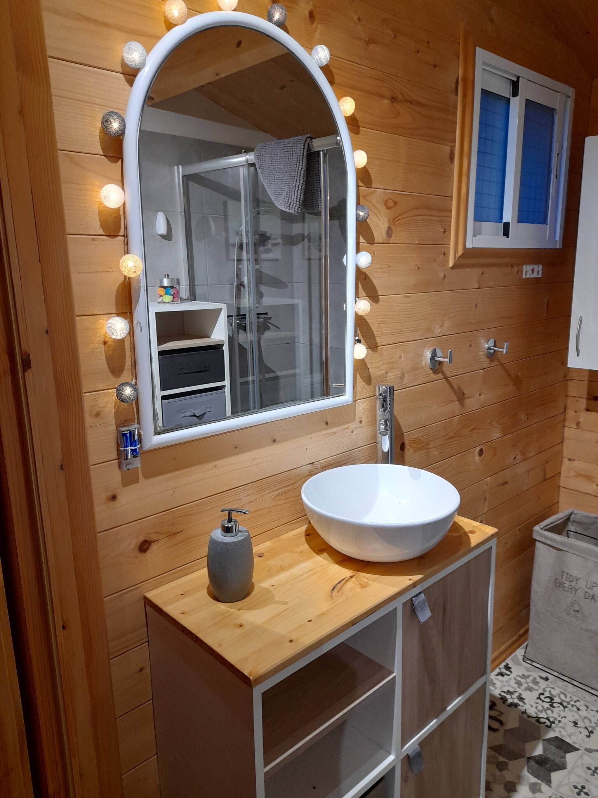 A wooden bathroom with a round mirror, a white sink, and a towel hanging on the wall.