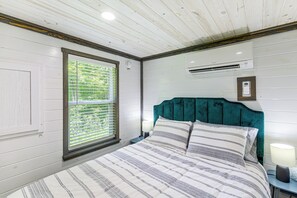 Ein Schlafzimmer mit einem Bett, einem Fenster mit Jalousien, einer Klimaanlage und einem Nachttisch mit Lampe.