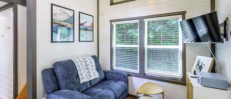 Una habitación con un sofá azul, una mesita, un televisor y una ventana con persianas.
