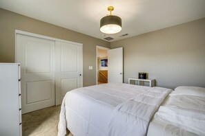 A bedroom with a large bed, a white wardrobe, a bedside table with a lamp, and a door leading to another room. - Stylish Family Home w/ Playground in Las Vegas (Las Vegas)