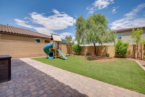 Un jardin avec une aire de jeux, une terrasse en briques et une pelouse.
