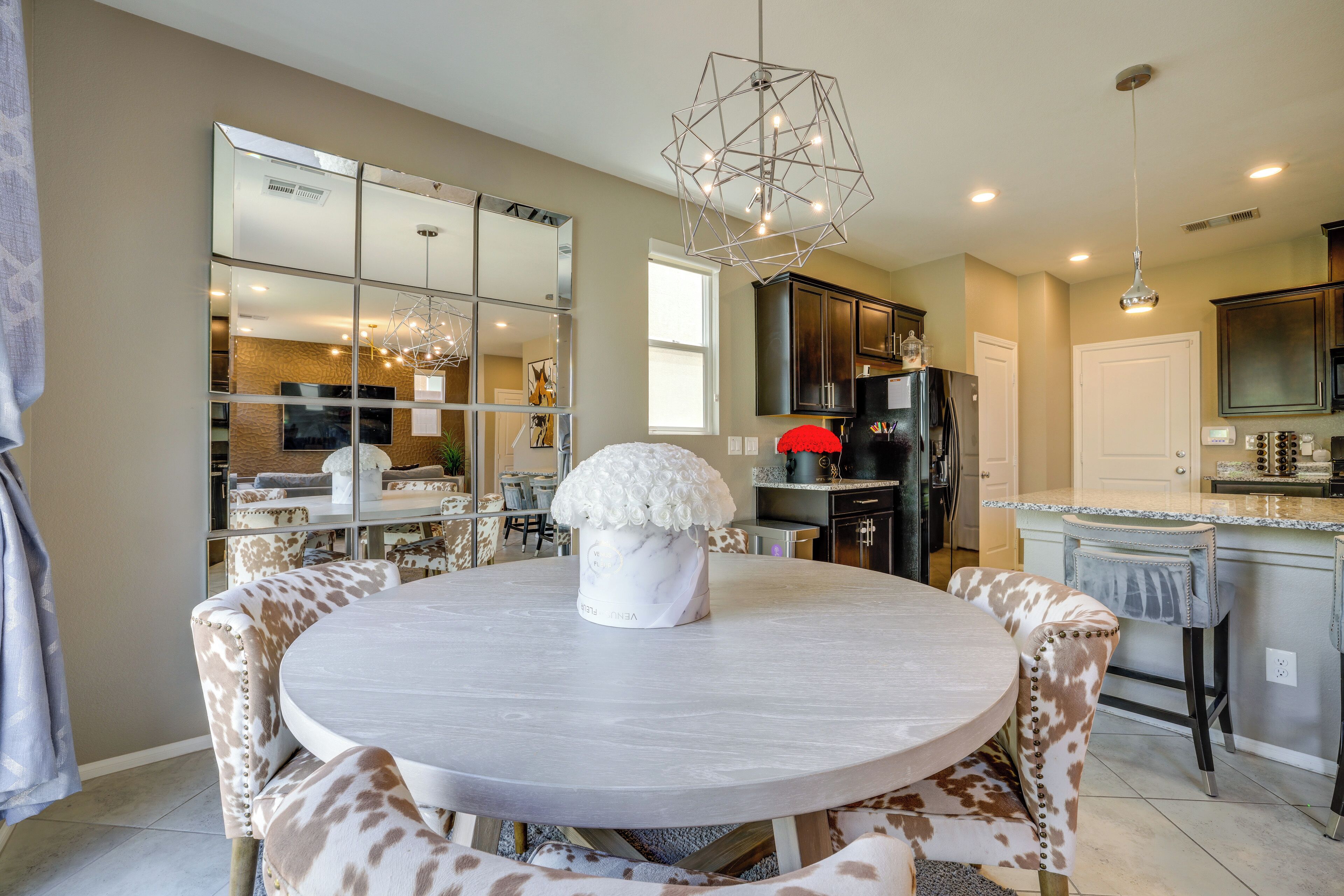 A modern kitchen with a round dining table, a chandelier, and a refrigerator.