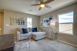 Ein Wohnzimmer mit Deckenventilator, einer Couch mit Kissen, einem Couchtisch, einem Beistelltisch mit Lampe, einem Wandspiegel und einem großen Fenster mit Blick.