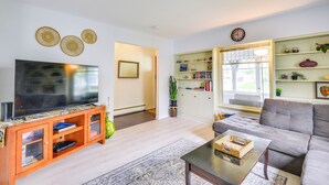 Ein Wohnzimmer mit Flachbildfernseher, einer Holz-Unterhaltungsecke, einem grauen Sofa und einem Couchtisch.