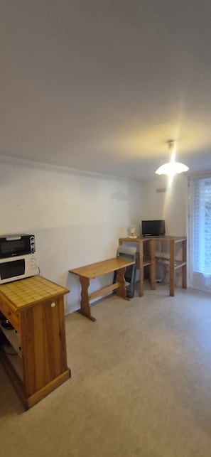 A room with a kitchenette, a wooden bench, a desk, a chair, and a television. - Studio dans les Pyrénées françaises (Esquièze-Sère)
