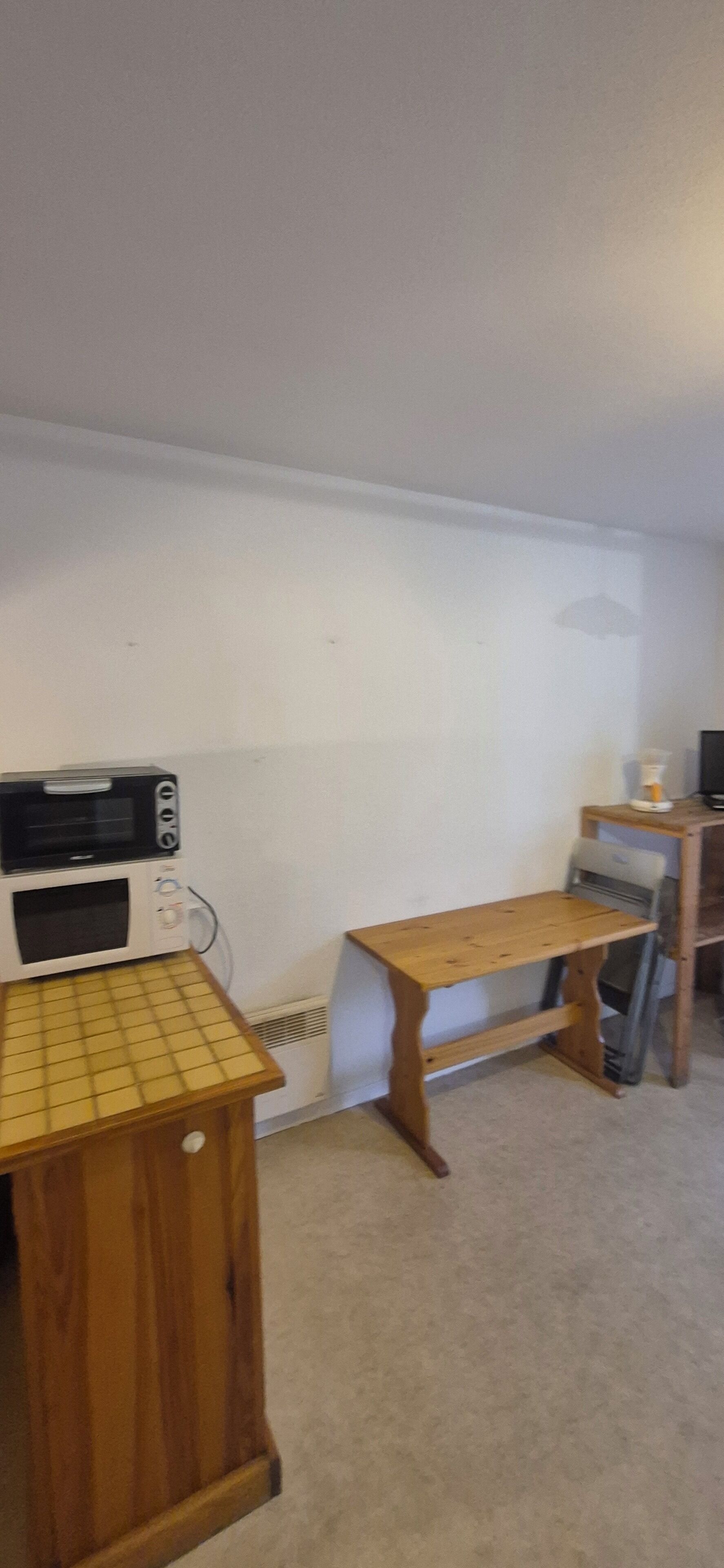 A room with a kitchenette area including a microwave, a small table, and a chair.