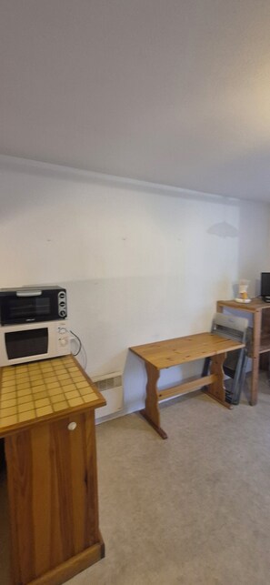A room with a kitchenette area including a microwave, a small table, and a chair. - Studio dans les Pyrénées françaises (Esquièze-Sère)
