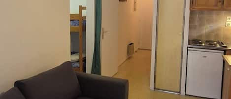 A compact living space with a sofa, a kitchenette, and a door leading to a hallway.